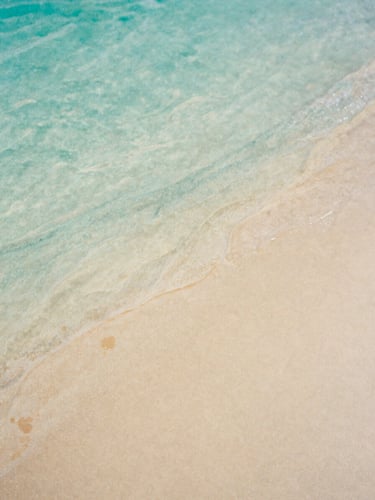 A close-up of soft watercolor textures, flowing turquoise and warm sand pigments blending gently on textured paper, natural daylight, 35mm