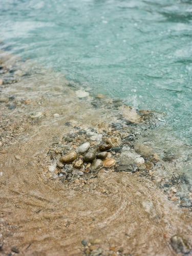 Soft close-up of clear flowing river water over smooth sand, diffused overcast daylight, calming turquoise tones, 35mm
