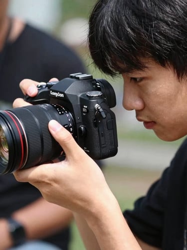 Candid close-up of a young person's hands operating a professional camera, a mentor's hand gently guiding, natural high-contrast daylight, dynamic composition showing focus and learning.