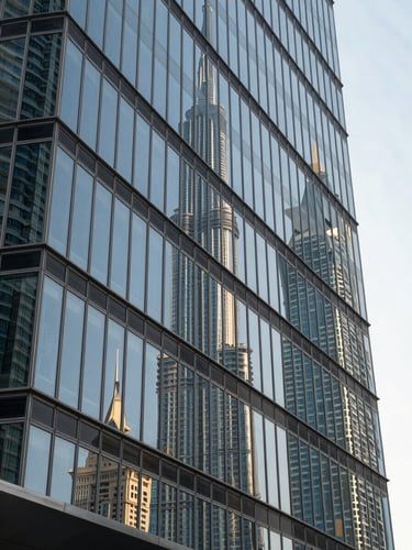 Close-up of a floor-to-ceiling glass facade on a Dubai commercial building, reflections of sky and neighbouring towers in even midday light, architectural lines receding to the upper right, no people, no signage