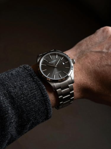 Tight wrist shot of a modern steel watch on a dark grey wool sleeve, directional side-lighting casting sharp highlights on the polished bezel.