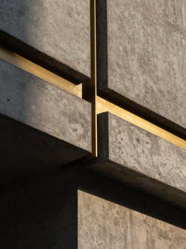 Extreme close-up architectural detail of raw concrete meeting warm brass trims, crisp natural light casting sharp geometric lines, minimalist luxury aesthetic.