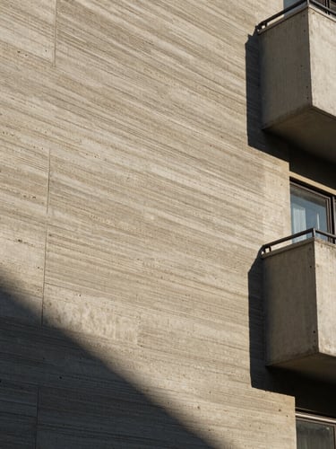 Primer plano de un muro residencial de concreto expuesto con textura de cimbra de madera, bañado por luz solar rasante que crea sombras profundas.