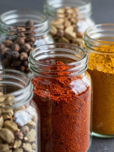 Close-up of glass jars filled with colorful South Asian spices like red chili powder, yellow turmeric, and whole cardamom pods, soft natural lighting.
