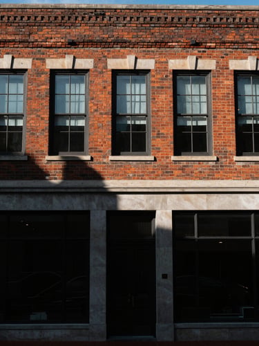 Sharp, high-contrast architectural crop of a historic brick commercial facade in Columbia SC, crisp afternoon sun casting deep shadows, clean glass windows.
