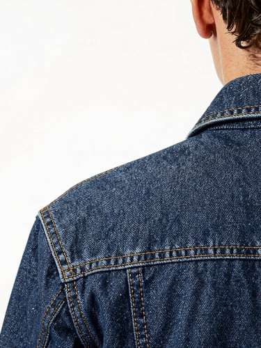 Professional quality control inspector examining a denim jacket under bright studio light, focusing on the collar seams, minimalist white background, 35mm