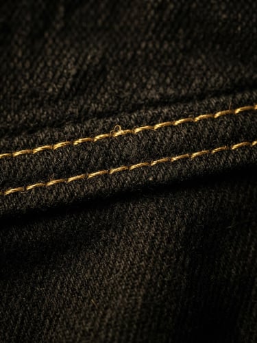 Tight macro crop of precise double-stitching on heavy black cotton garment, golden studio lighting, sharp details, 35mm