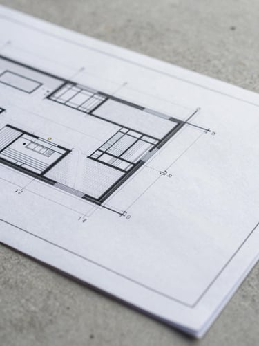 Crisp macro photograph of a detailed architectural blueprint showing structural junctions and thermal envelope details, laid over a desaturated concrete background.