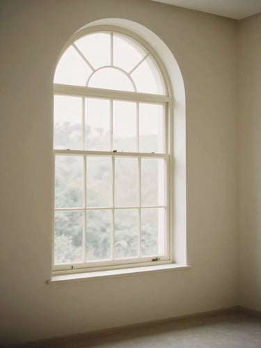 Soft diffused natural daylight entering a calm room through a large arched window, minimalist interior with warm cream tones, 35mm photography