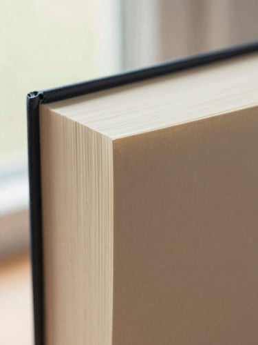 Extreme close-up of book spine binding threads and heavy textured cream paper grain, soft diffused natural light, warm tones.