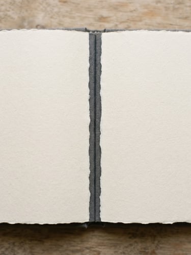 Macro overhead shot of an open linen-bound book under soft window light, showing the heavy cream paper texture and crisp monotype letterpress typography, shallow depth of field.