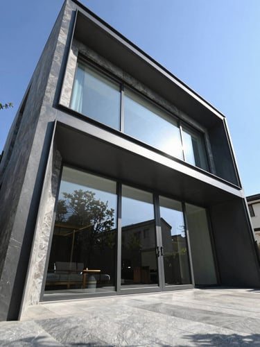 Low-angle architectural photography of a modern luxury villa facade with huge minimalist sliding glass doors and dark slate aluminum profiles, sharp shadows, bright daylight