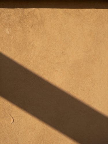 Dramatic natural daylight casting sharp architectural shadows across a textured, warm plaster wall, minimalist composition revealing true paint sheen