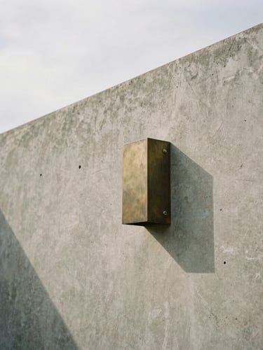 Tight architectural crop of low-contrast overcast daylight hitting a raw concrete wall and cast bronze fixture, soft natural shadows, 35mm film