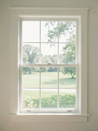 Bright sun-drenched home interior with a large clean window framing a soft green Iowa yard, morning light, architectural framing