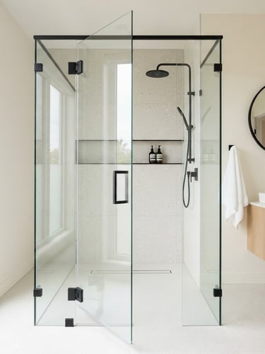 Straight-on architectural photography of a bright modern bathroom featuring a custom frameless glass shower enclosure with matte black hardware, natural daylight reflecting off the polished glass edge, sharp focus, 35mm lens