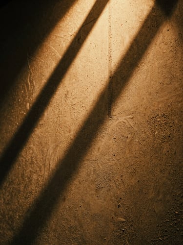 Extreme close-up of a warm light fixture casting dramatic shadows on raw textured concrete, grainy film texture, 35mm lens