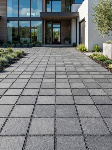 Crisp architectural photography of a modern residential driveway with perfectly aligned gray basalt paving stones, bright afternoon daylight, clean geometric alignment, sharp stone textures, no people.