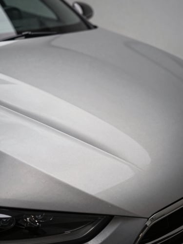 Extreme close-up of paint protection film being laid across a sculpted hood panel in a controlled studio environment, studio strobe lighting raking across the surface to reveal the film's near-invisible edge — cool neutral light, no warmth, surface texture dominant in frame