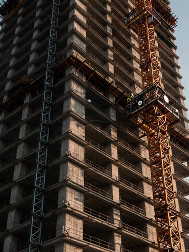 Low-angle dramatic shot of a massive high-rise construction site, heavy-duty steel shoring towers supporting a concrete floor pour, high-contrast industrial lighting, cool metallic tones with warm sunset highlights, 35mm