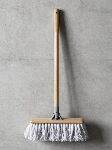 A solid ash mop handle resting against a clean, raw concrete wall, sharp studio shadows highlighting the wood grain, neutral tones, high contrast, 50mm