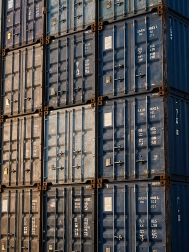Close-up detail of steel shipping containers stacked neatly in a modern logistics terminal, morning sunlight, high-contrast industrial photography, 35mm.