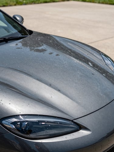 Close-up of water perfectly beading on a dark grey ceramic-coated sports car hood in a clean driveway, sharp natural daylight
