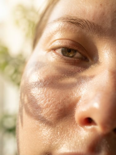 A close-up of fresh dewy skin with morning window light reflecting soft golden tones, natural pores and radiant texture visible, botanical leaf shadow.