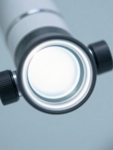 Macro shot of a modern ophthalmic diagnostic lens reflecting bright, clean clinical white light, with a soft slate blue background.