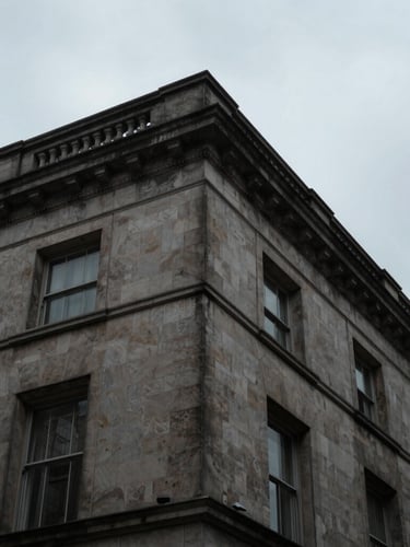 Extreme low-angle architectural crop of a Portland stone building corner against a moody overcast London sky, sharp focus
