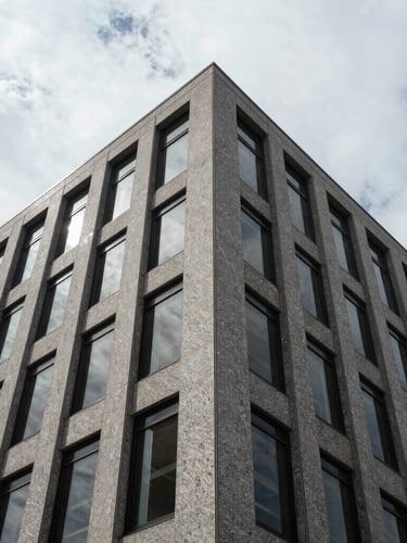 Low-angle architectural crop of a granite and glass corporate facade in Wilmington, stark shadows, high-contrast overcast daylight.