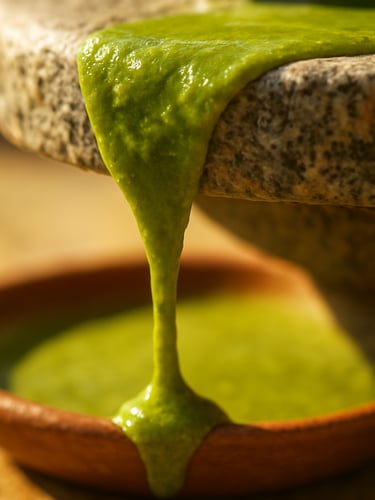 Macro close-up of vibrant green stone-ground pistachio paste dripping slowly from a granite millstone, bright warm Mediterranean sunlight, shallow depth of field.