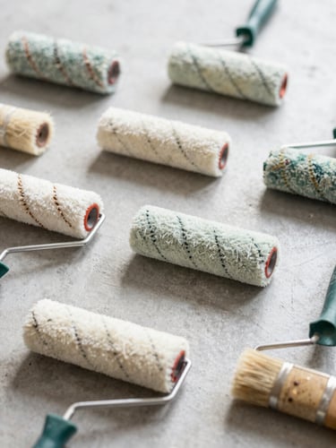 Close-up of clean paint rollers and brushes arranged neatly on a light gray concrete surface, soft natural shadows, 35mm lens