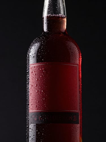Low-angle heroic product shot of a sleek, condensation-covered custom glass bottle with a dark crimson label, dramatic studio lighting, deep shadows, 85mm.