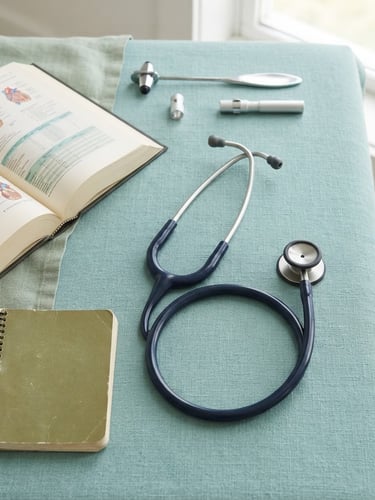 Clean flat-lay of medical guides and stethoscope on a soft teal surface, bright natural daylight, sharp focus, professional clinical setting