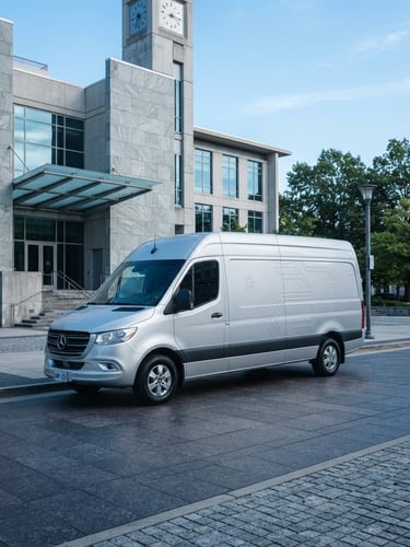 A clean silver transit vehicle with subtle professional branding parked outside a modern stone courthouse, bright daylight, cool blue tones.