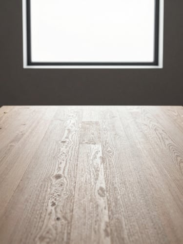 Minimalist close-up of a modern boardroom table made of light oak, subtle brass fittings, clean architectural lines, soft side lighting from a large window