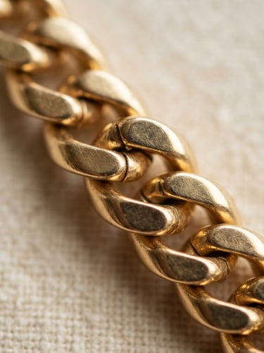 Macro close-up of heavy interlocking gold chain links, soft natural side-light, warm ivory background, 35mm