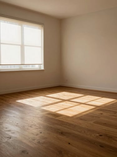 Wide environmental shot of a living room interior, soft north-facing daylight streaming through roller blinds casting diffused shadow bands across warm engineered wood flooring, empty room with no people, window furnishings and floor grain both clearly visible and in tonal conversation, muted warm neutrals throughout