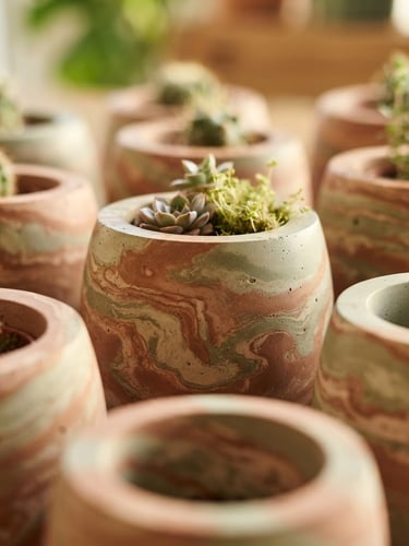 Macro shot of hand-cast concrete planters with swirling terracotta and sage green mineral pigments, warm morning light, soft shadows, sharp focus on flawless silky texture
