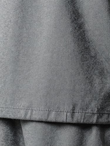 Extreme close-up of heavy-weight cotton fabric texture, double-stitched hem details, cold overcast studio lighting, desaturated grey tones, high-contrast.
