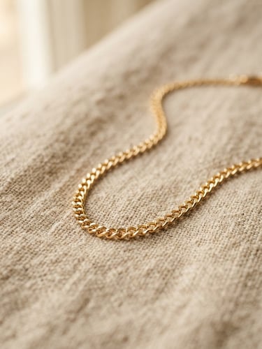 Macro detail shot of a gold-plated chain necklace resting on textured sand linen, soft natural window light, warm editorial styling
