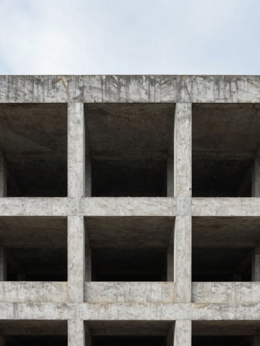 Straight-on architectural framing of an exposed concrete building structure under overcast daylight, sharp geometric lines, unvarnished site reality.