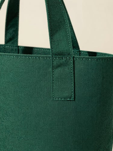 Macro detail of a deep forest green nonwoven bag handle, showing clean ultrasonic weld seams and raw spunbond fabric texture under bright daylight