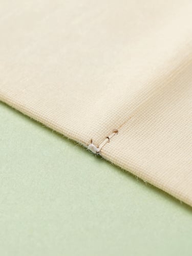 Macro detail shot of a clean ultrasonic weld seam on a raw canvas cream nonwoven bag, showing fused spunbond fabric texture, soft industrial studio lighting
