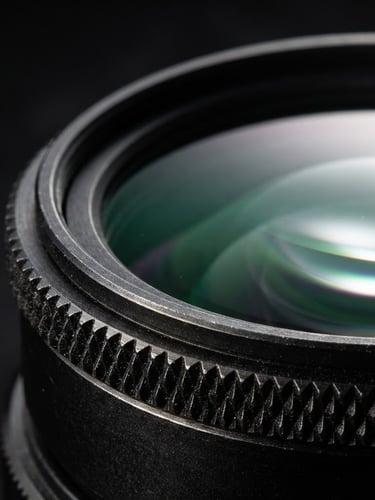 Extreme macro shot of a pristine camera filter glass element, subtle green and purple anti-reflective coatings reflecting a sharp studio rim light, dark metallic knurled ring, 85mm