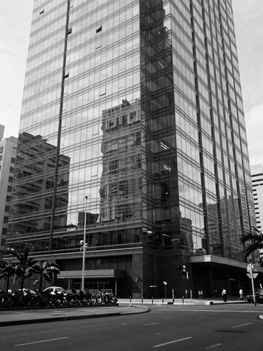 Wide environmental shot of a Luanda business district facade reflected in glass, angular geometry, empty foreground, controlled daylight, black and white, architectural precision