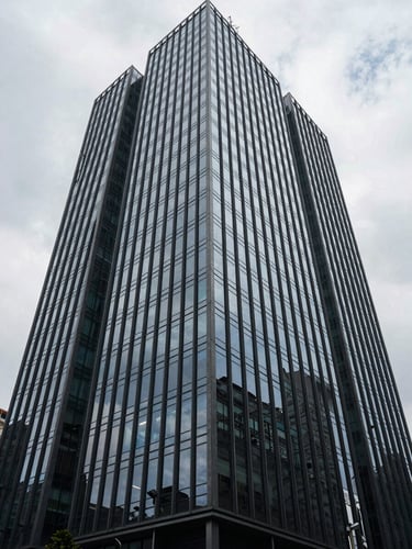 Wide shot from street level looking up at a modern Luanda commercial tower, glass facade reflecting overcast sky, geometric grid of windows receding to upper right, controlled natural light, no people visible, architectural precision