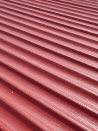 Bold industrial photography of high-contrast corrugated red steel roofing sheets under direct bright sunlight, sharp focus on metallic texture