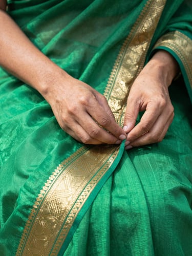 Close-up of hands feeling a rich emerald green silk saree with intricate gold zari border, bright natural daylight, shallow depth of field
